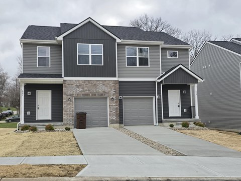 A grey house with a white door and a brown trash can.